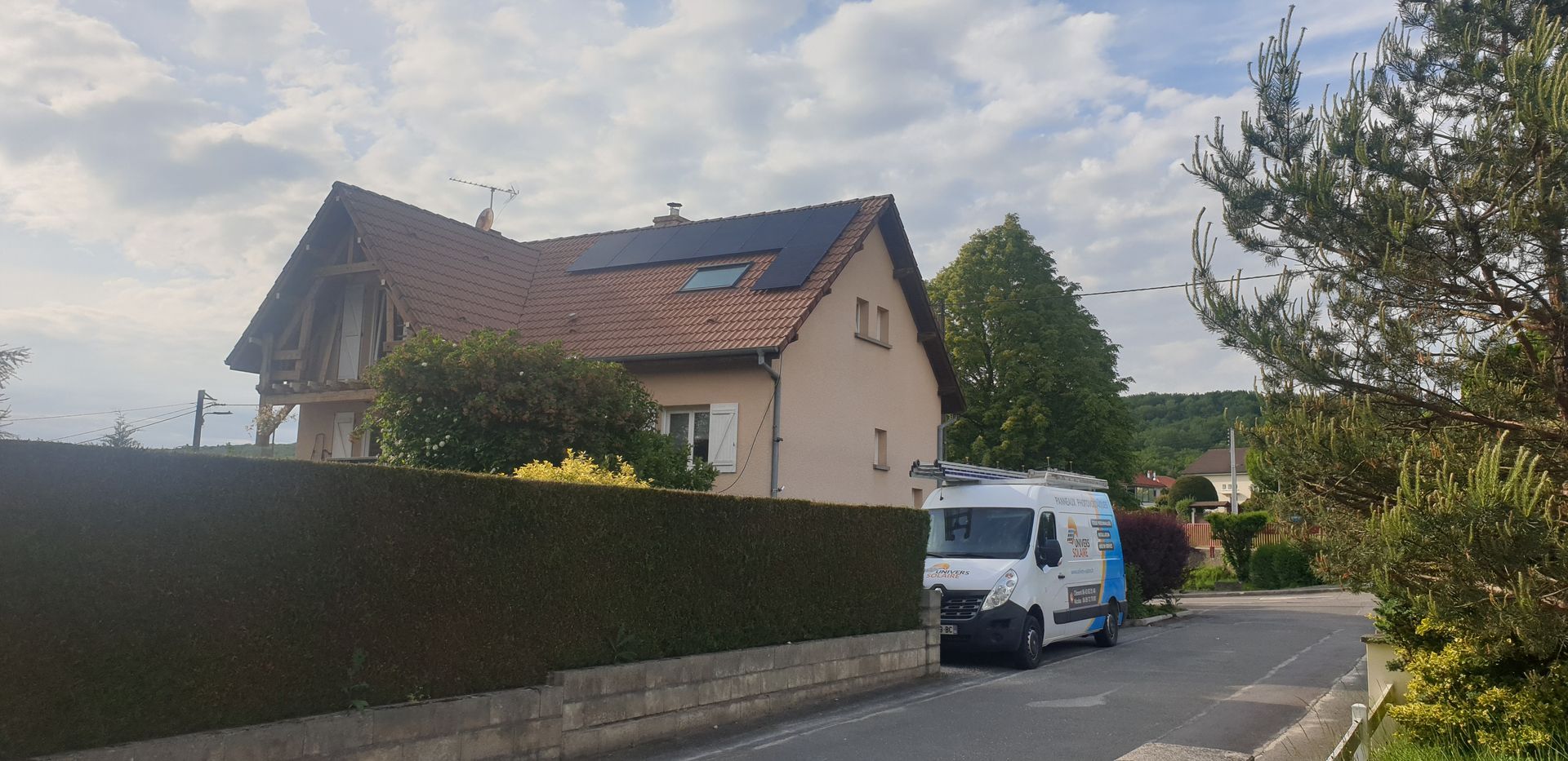Photo d'une maison vue de biais avec des panneaux solaires sur le toit et le camion de l'entreprise devant la maison