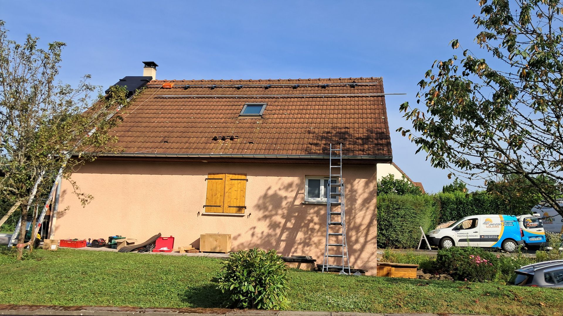 Photo d'une maison rose avec des panneaux solaires en train d'être installés sur le toit à gauche