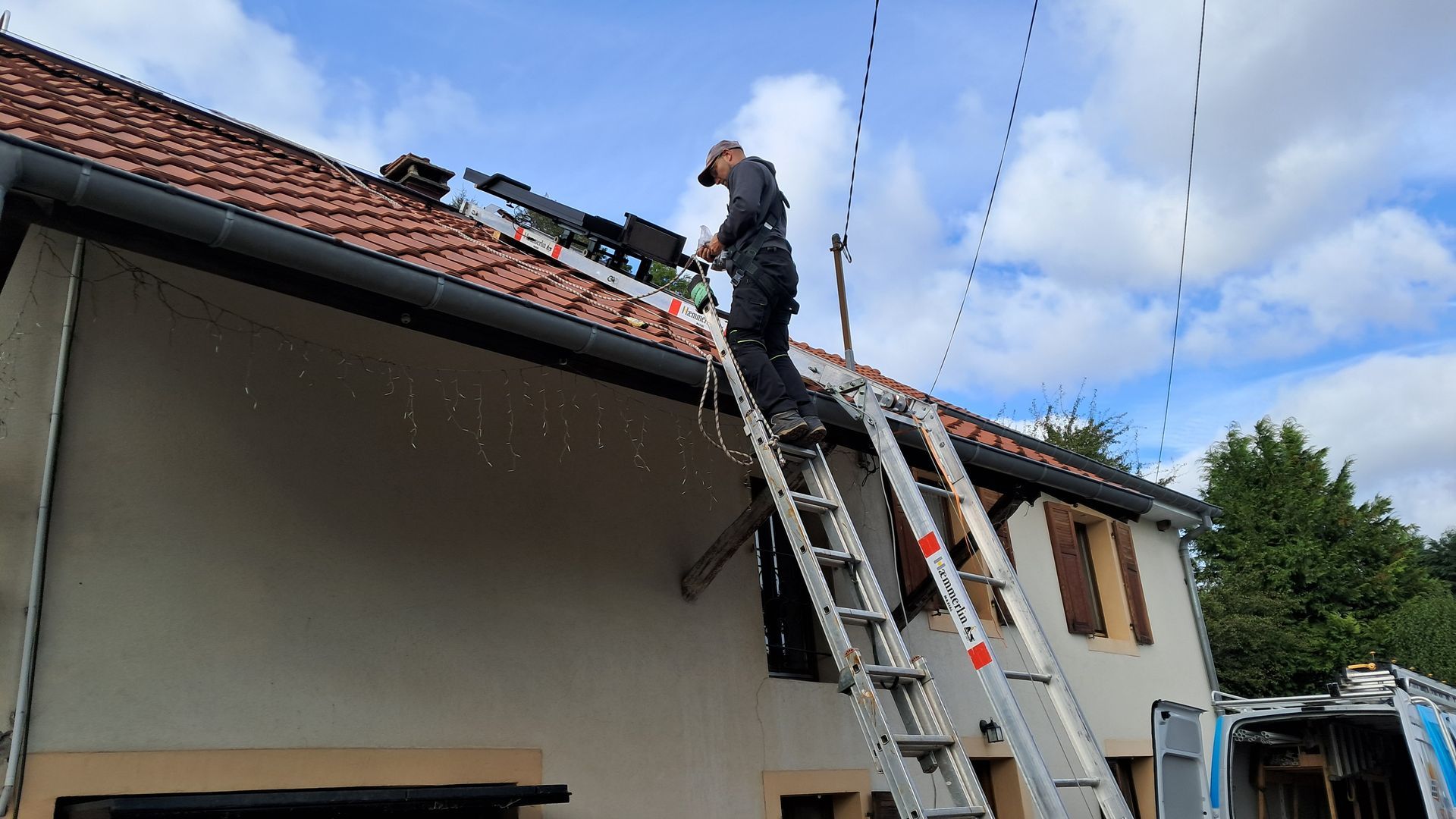 Photo d'un artisan sur une échelle, en train d'installer un panneau solaire sur le toit d'une maison