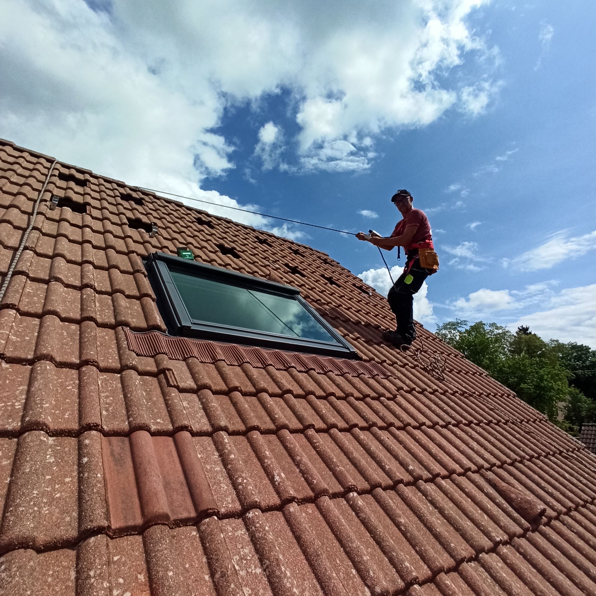 Photo d'un artisan sur le toit d'une maison, en train de s'agripper à la corde de sécurité