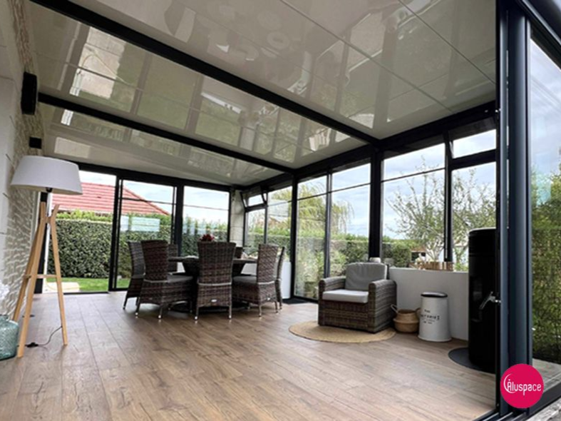 Véranda avec parois vitrées, parquet et mobilier, donnant sur un jardin verdoyant.