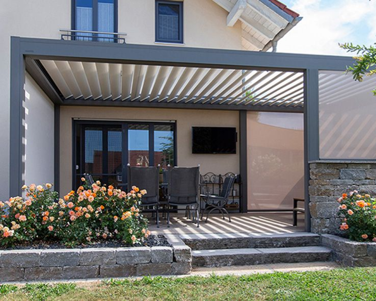 Patio avec pergola grise, coin salon et rosiers.