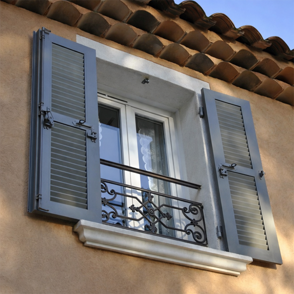 Fenêtre à volets gris, cadre blanc et appui de fenêtre en pierre, contre un mur clair.