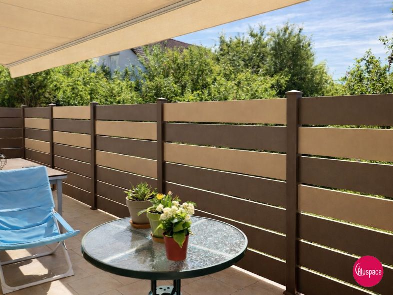 Terrasse avec une clôture horizontale bicolore, une table ronde, une chaise bleue et un auvent rayé.