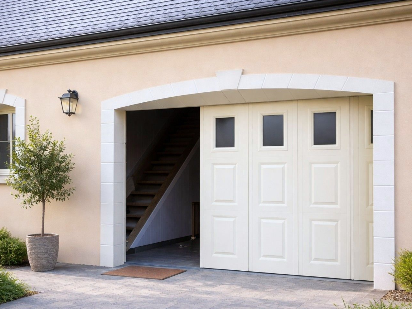Porte de garage beige ouverte. Vélo garé à l'extérieur. Escalier visible à l'intérieur du garage.