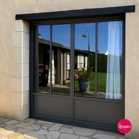 Vue extérieure d'une porte coulissante en verre à cadre gris, reflétant une maison et un ciel bleu.