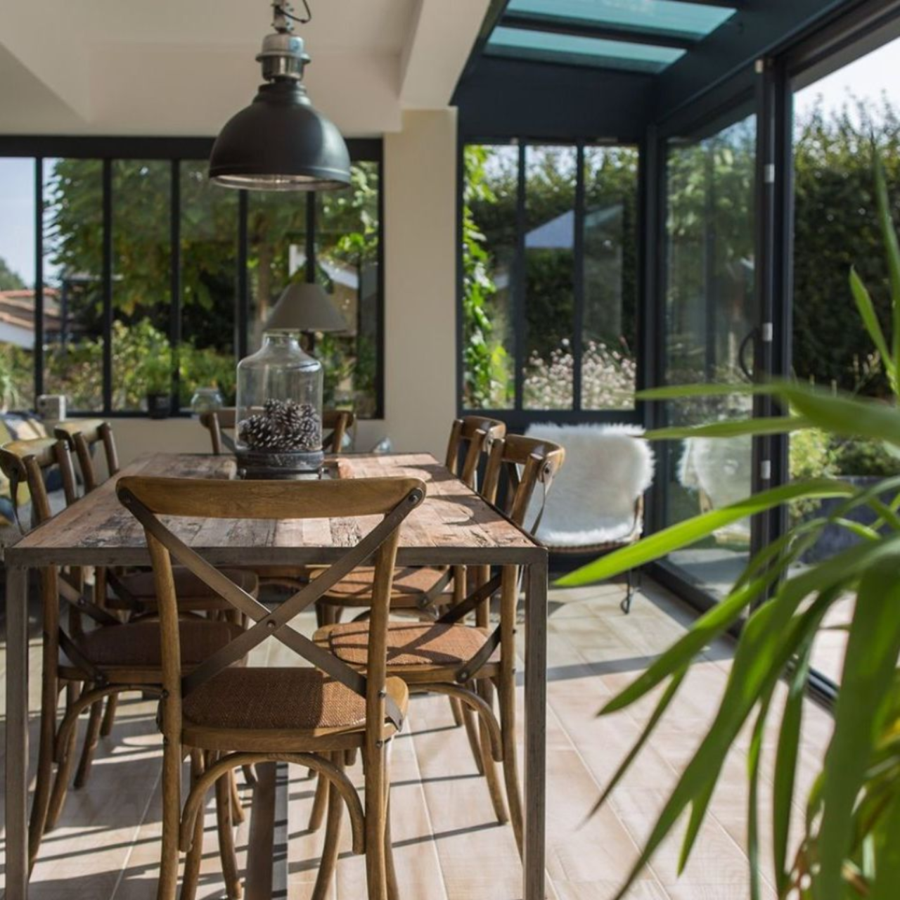 Salle à manger avec table en bois, chaises et grandes fenêtres donnant sur un jardin.