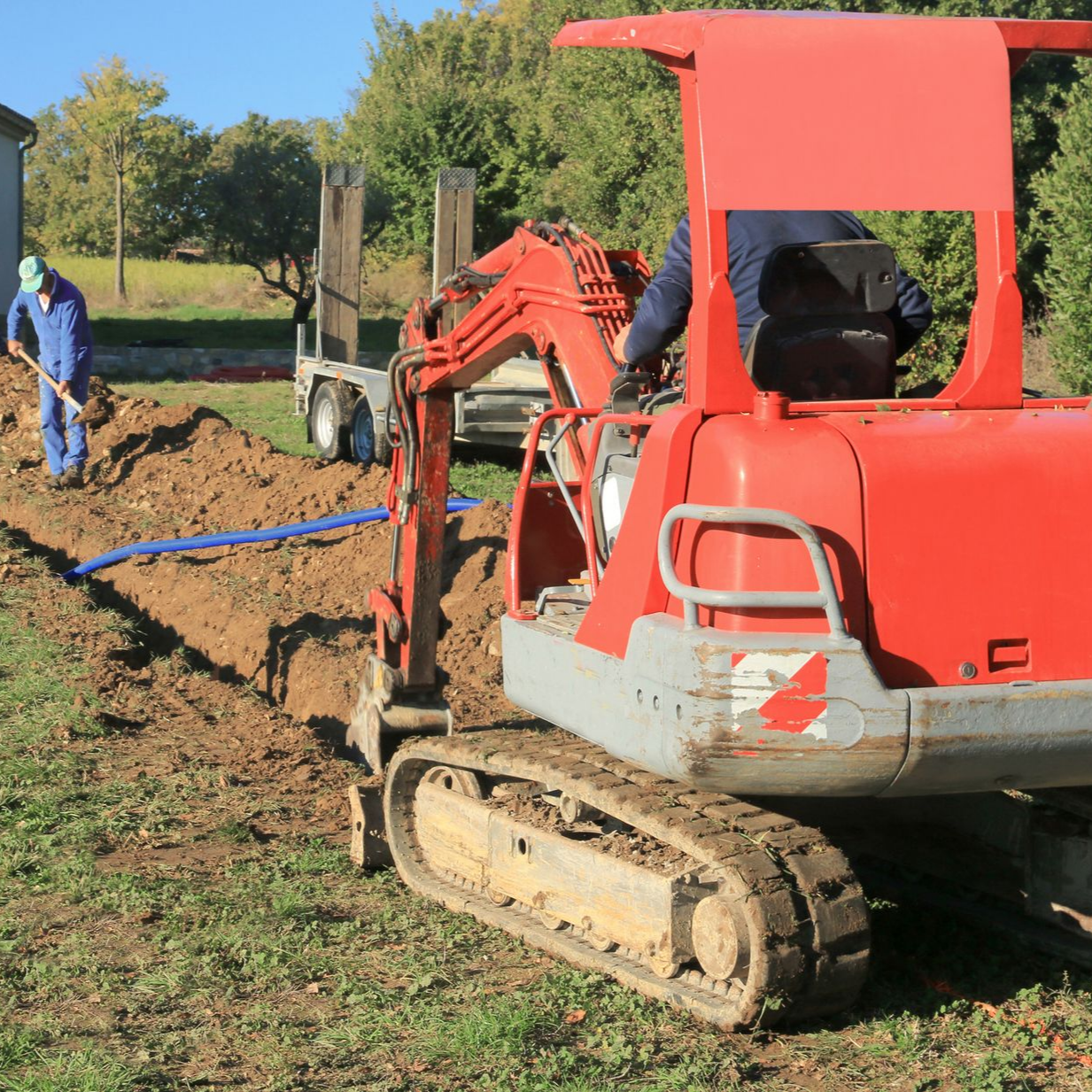 Une tractopelle creuse une tranchée pour un raccordement de l'électricité et d'internet.