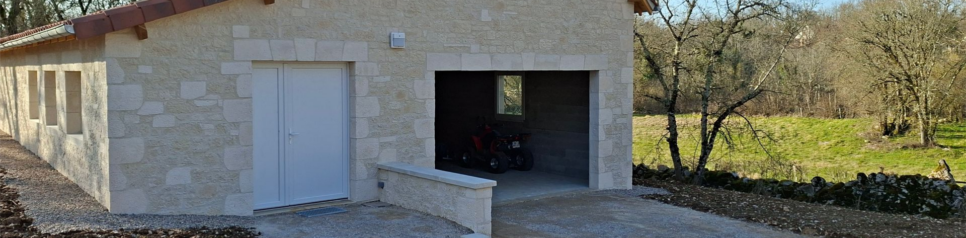 Un garage de plain-pied en pierre claire, avec une double porte blanche et un espace ouvert.