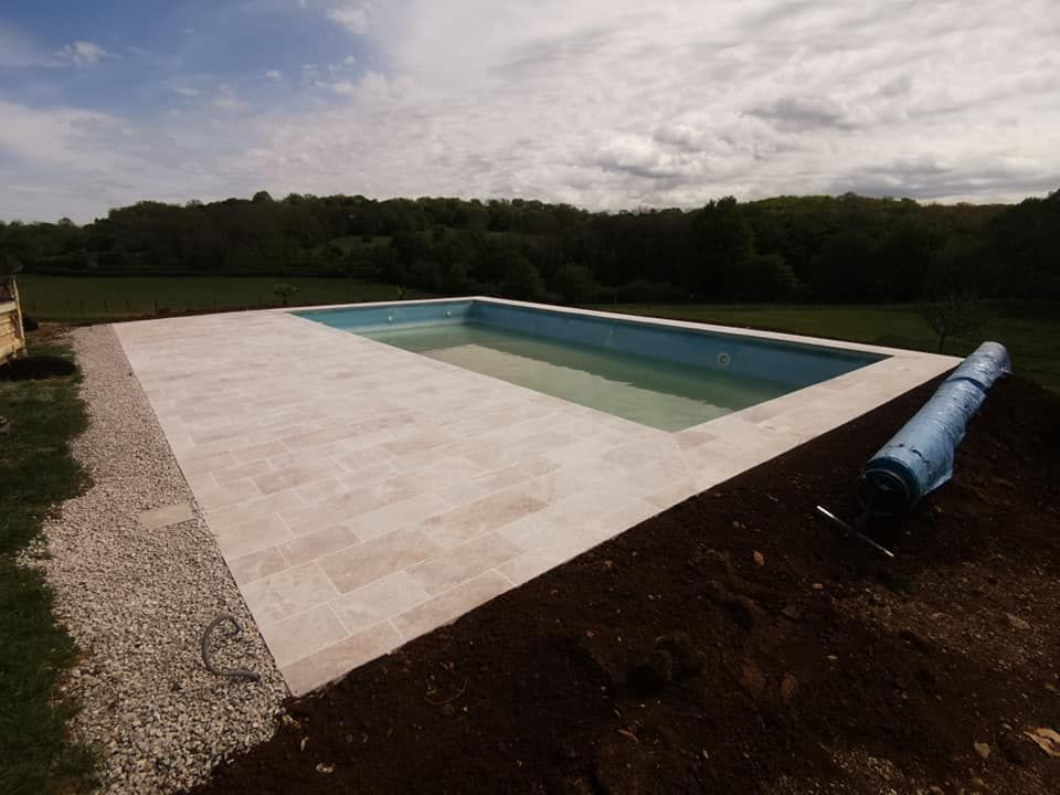 Une piscine installée avec une terrasse en dalles de pierre claire.