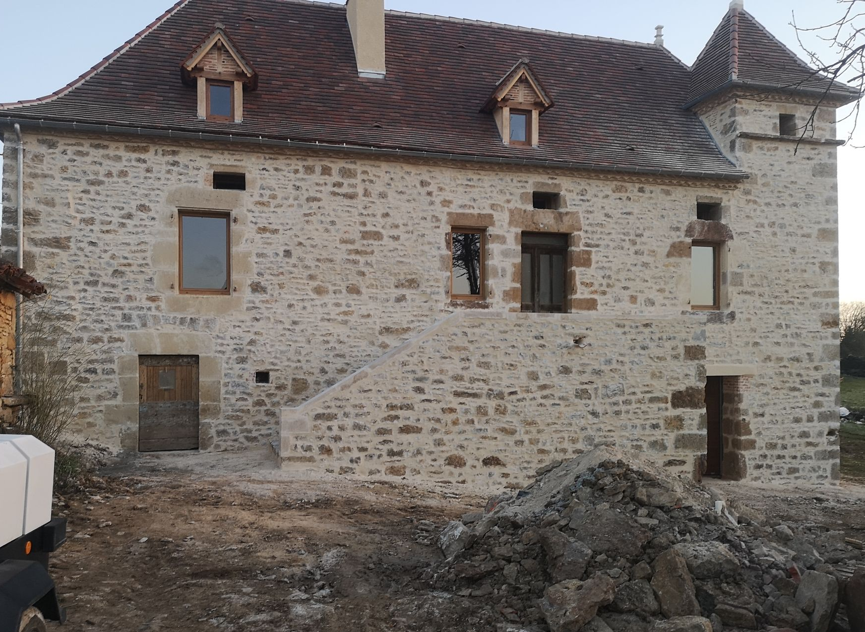 Une maison en pierre avec un toit de tuiles, une tourelle, des lucarnes et un escalier extérieur en pierre.