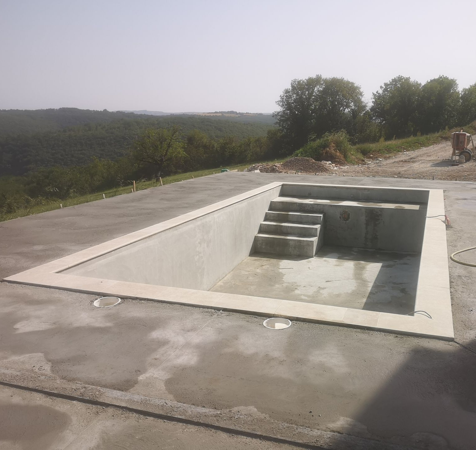 Une piscine rectangulaire en béton inachevée, avec escalier intégré.