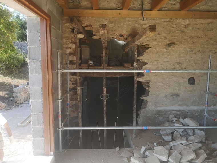 Un mur de pierre est en cours de rénovation ; des échafaudages et des supports métalliques soutiennent la structure.