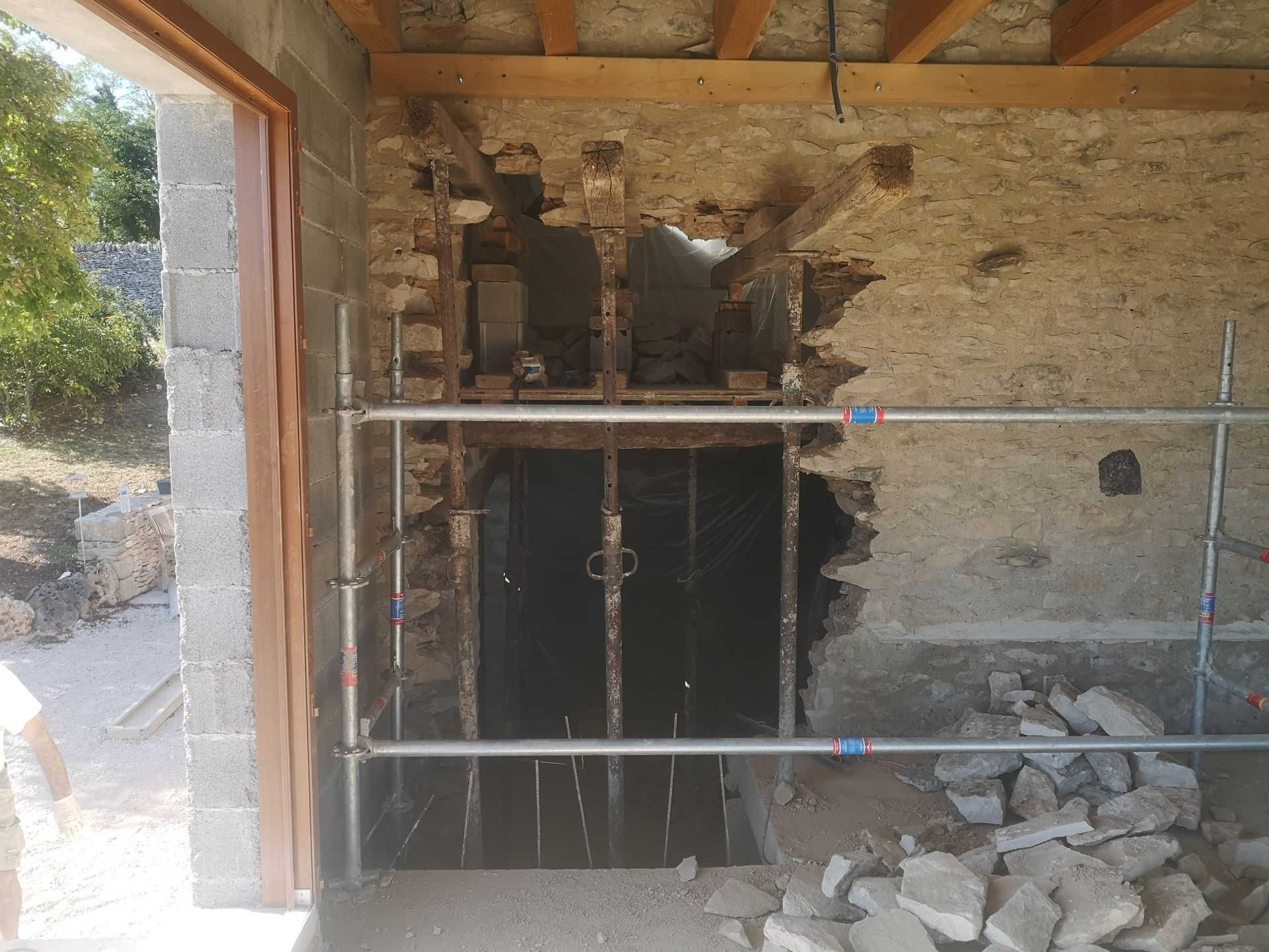 Chantier de construction à l'intérieur d'un bâtiment en pierre inachevé, avec des échafaudages soutenant l'ouverture.