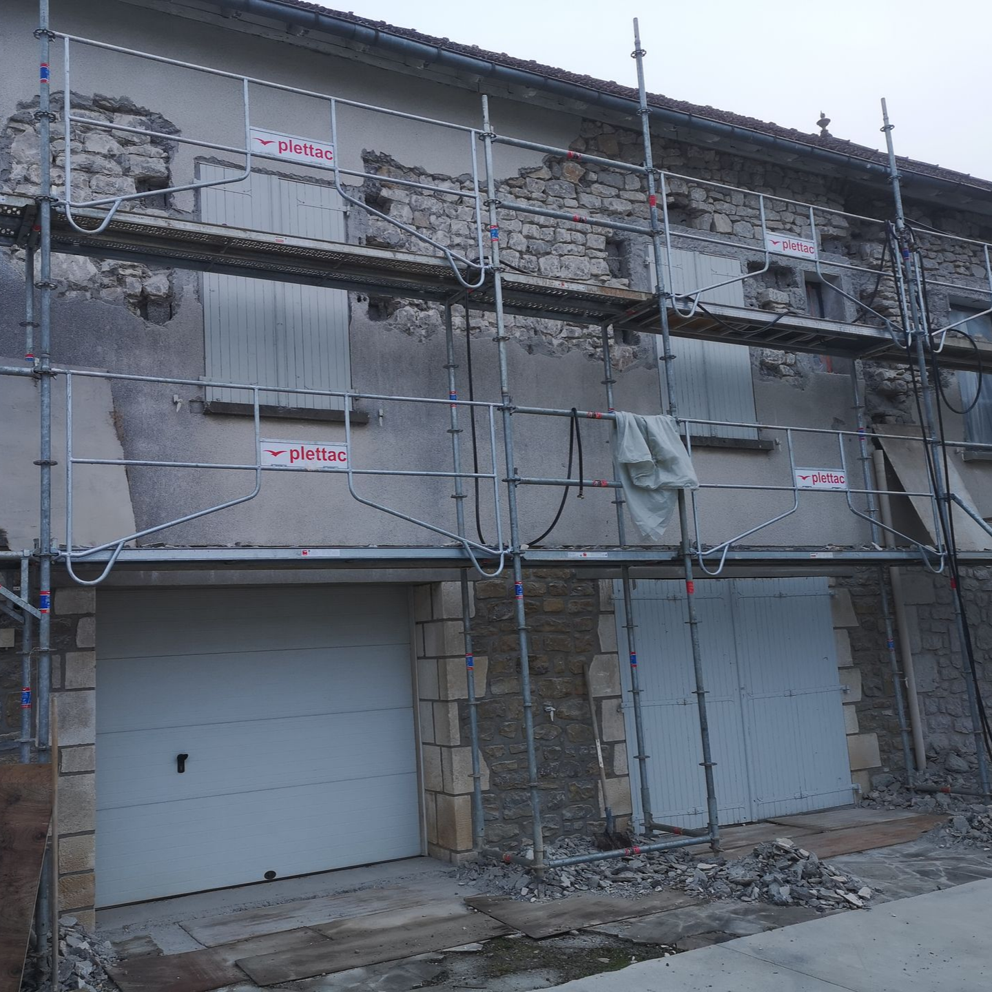 Façade d'une maison en pierre en cours de rénovation, partiellement décapée, entourée d'échafaudages métalliques.