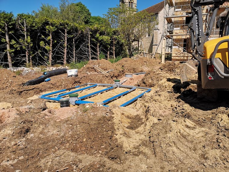 Des ouvriers du bâtiment installent un système de tuyaux de drainage bleus dans une tranchée de terre.