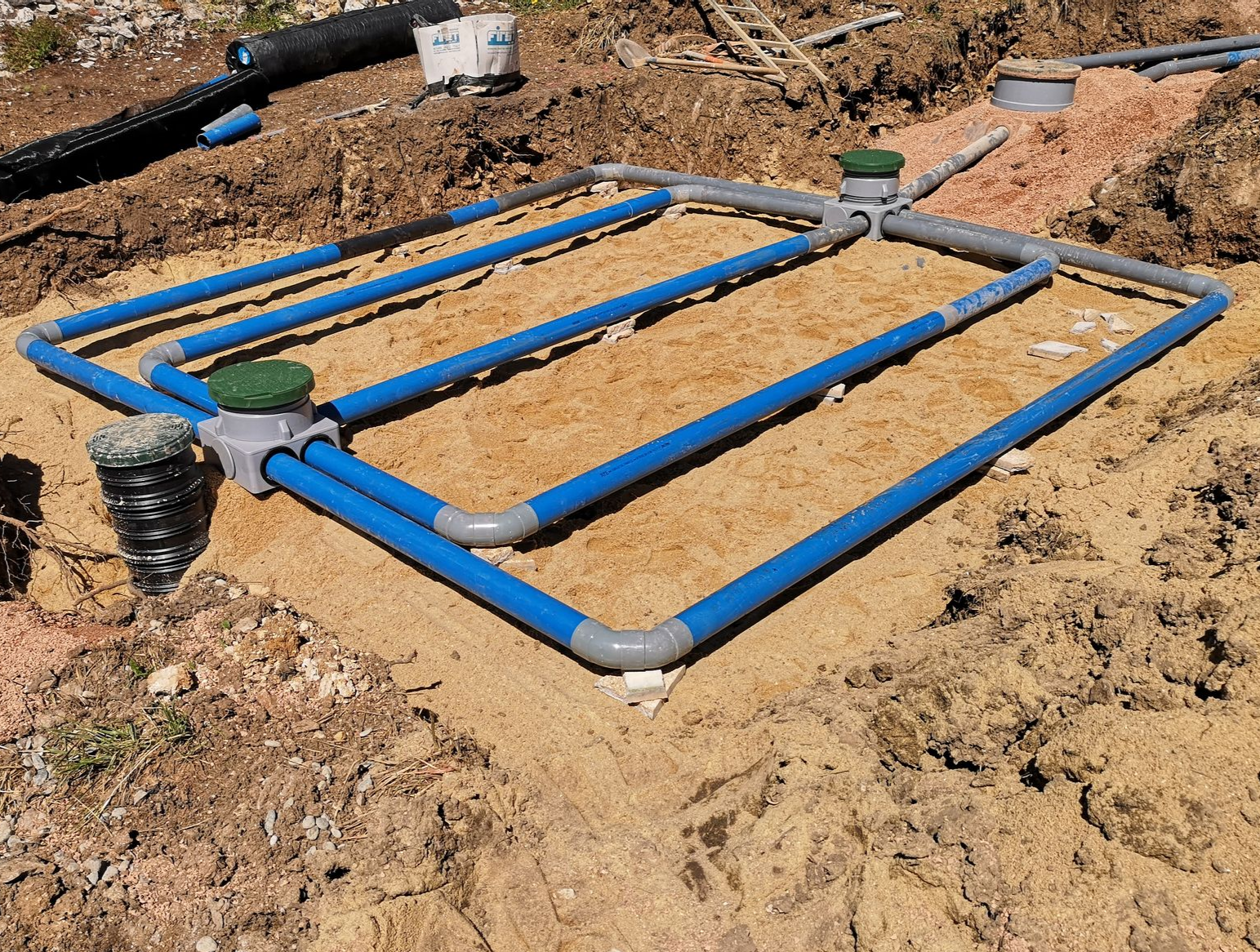 Un collecteur d'irrigation, avec des tuyaux bleus et des couvercles de vannes installé dans une tranchée.