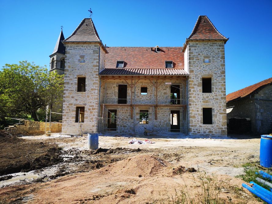Un manoir en pierre avec deux tours et un toit de tuiles rouges, en cours de rénovation.