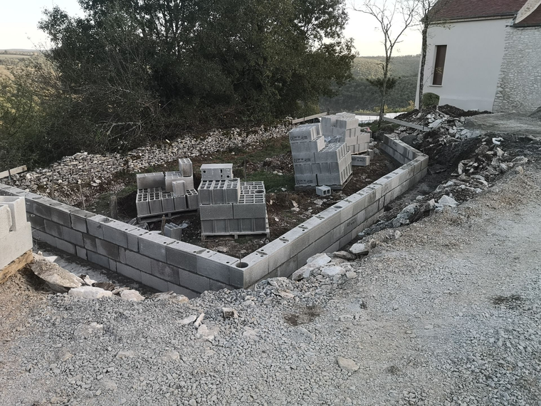Un muret en parpaings, bas et partiellement construit, se dresse sur un terrain gravillonné.