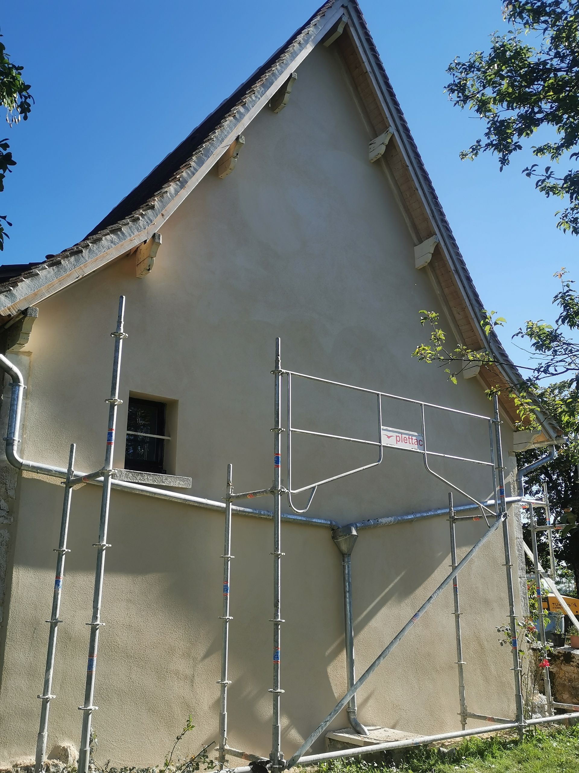 Un mur de maison clair, à pignon triangulaire masqué par des échafaudages métalliques.