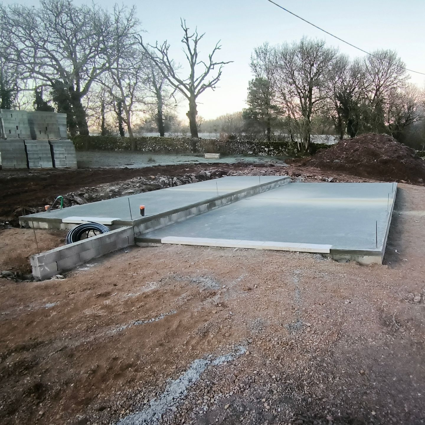 Fondations en béton fraîchement coulées d'un projet de construction reposant sur un terrain gravillonné.