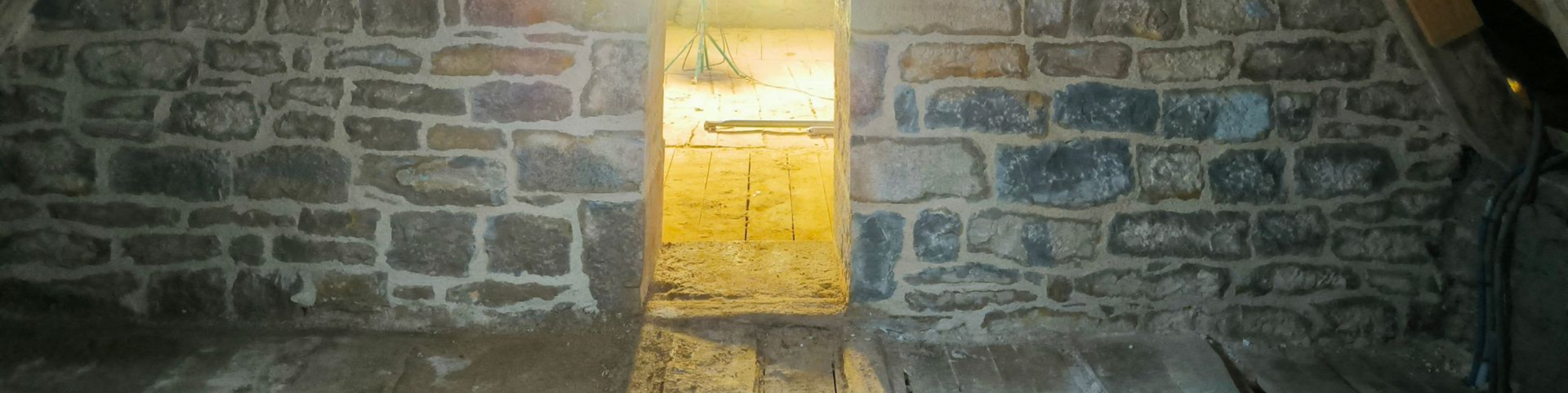 Un mur de pierre présente une porte ouverte donnant sur une pièce.