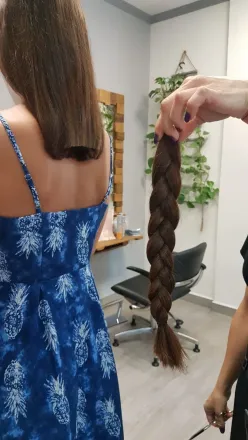 Mujer con vestido azul; larga trenza de cabello castaño recogida después del corte de pelo en el salón.
