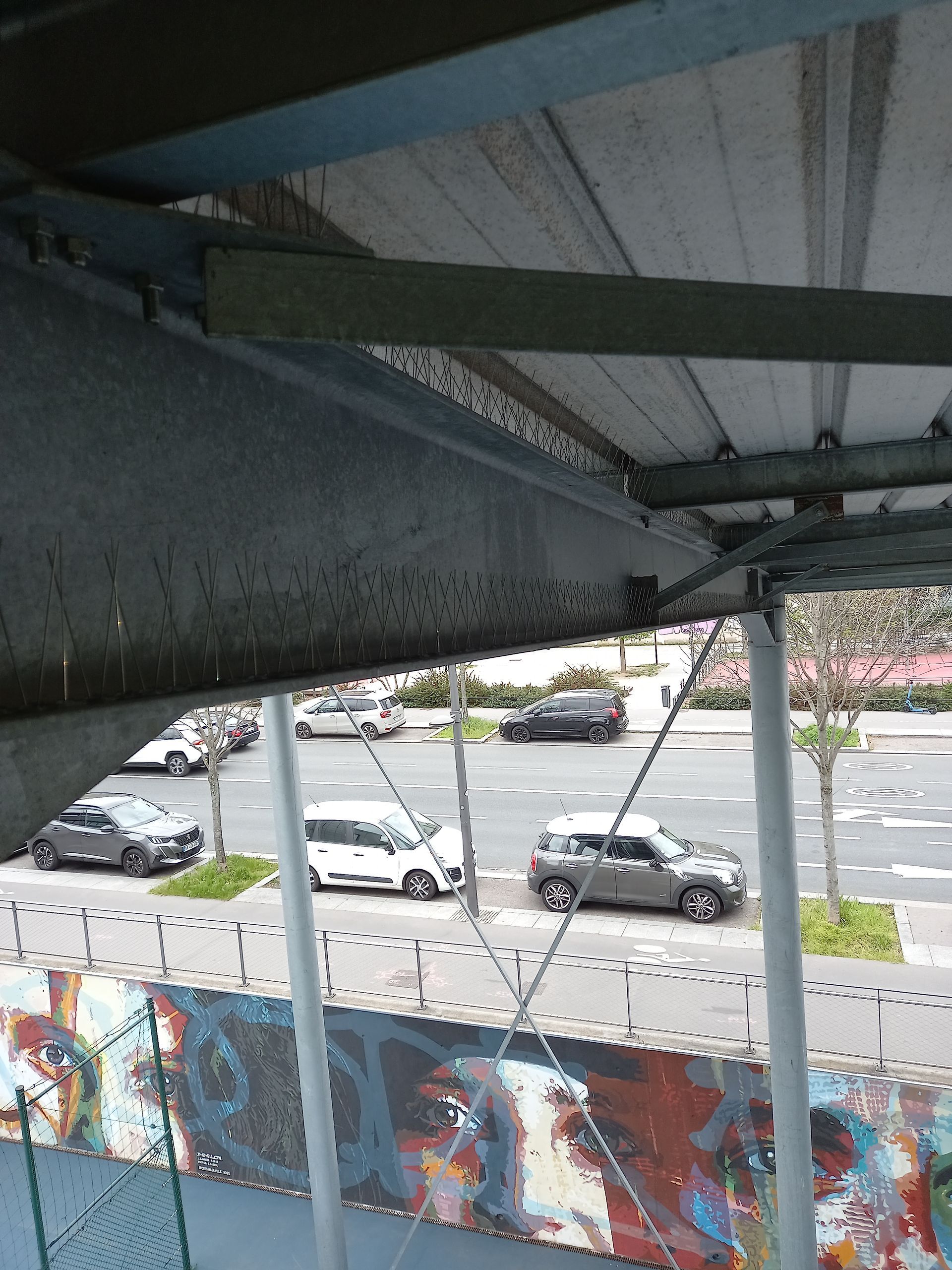 Présentation d'une pose de pic antipigeons sous le toit d'un gymnase air libre.