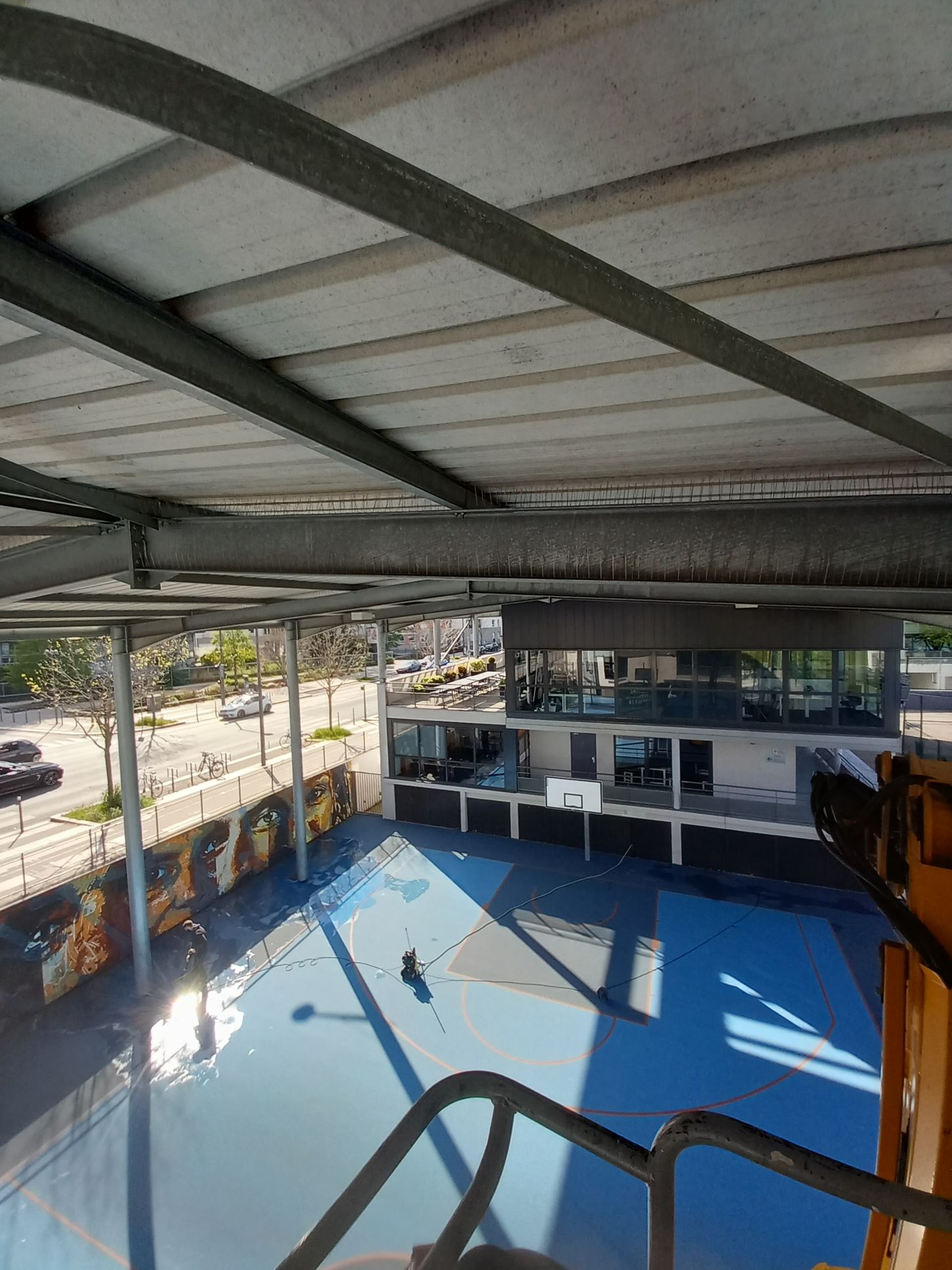 Présentation d'une pose de pic antipigeons sous le toit d'un gymnase air libre.