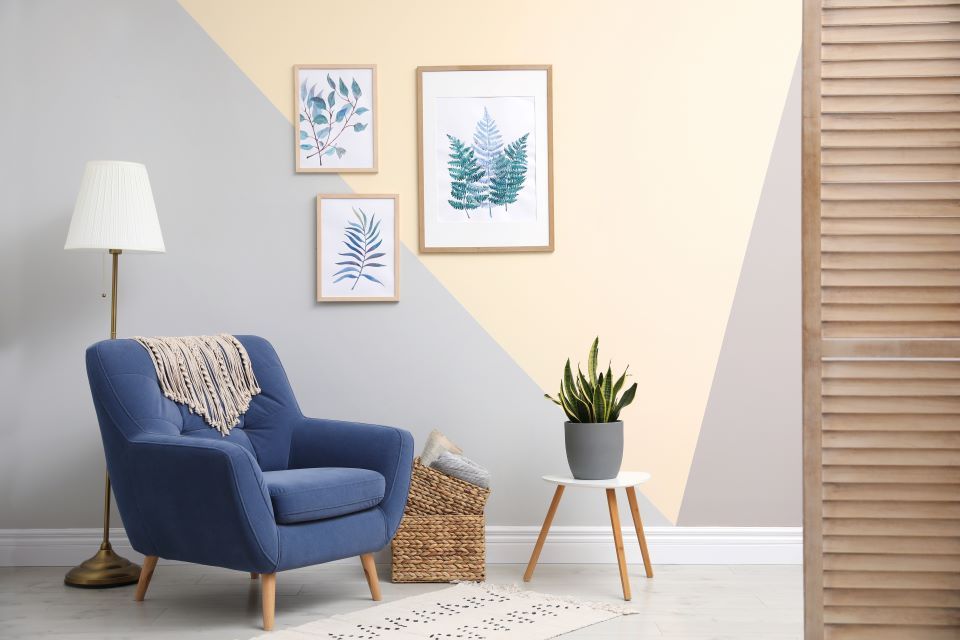Ein Wohnzimmer mit einem blauen Stuhl, einer Lampe, einem Tisch und Gemälden an der Wand.
