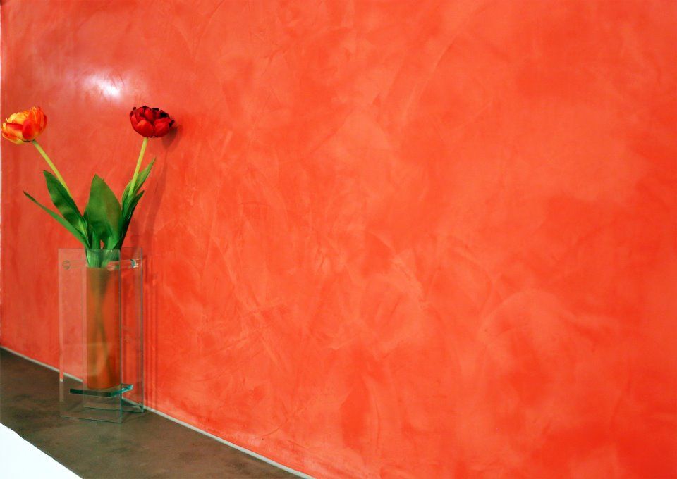 Eine Vase mit Blumen steht auf einem Tisch vor einer roten Wand.