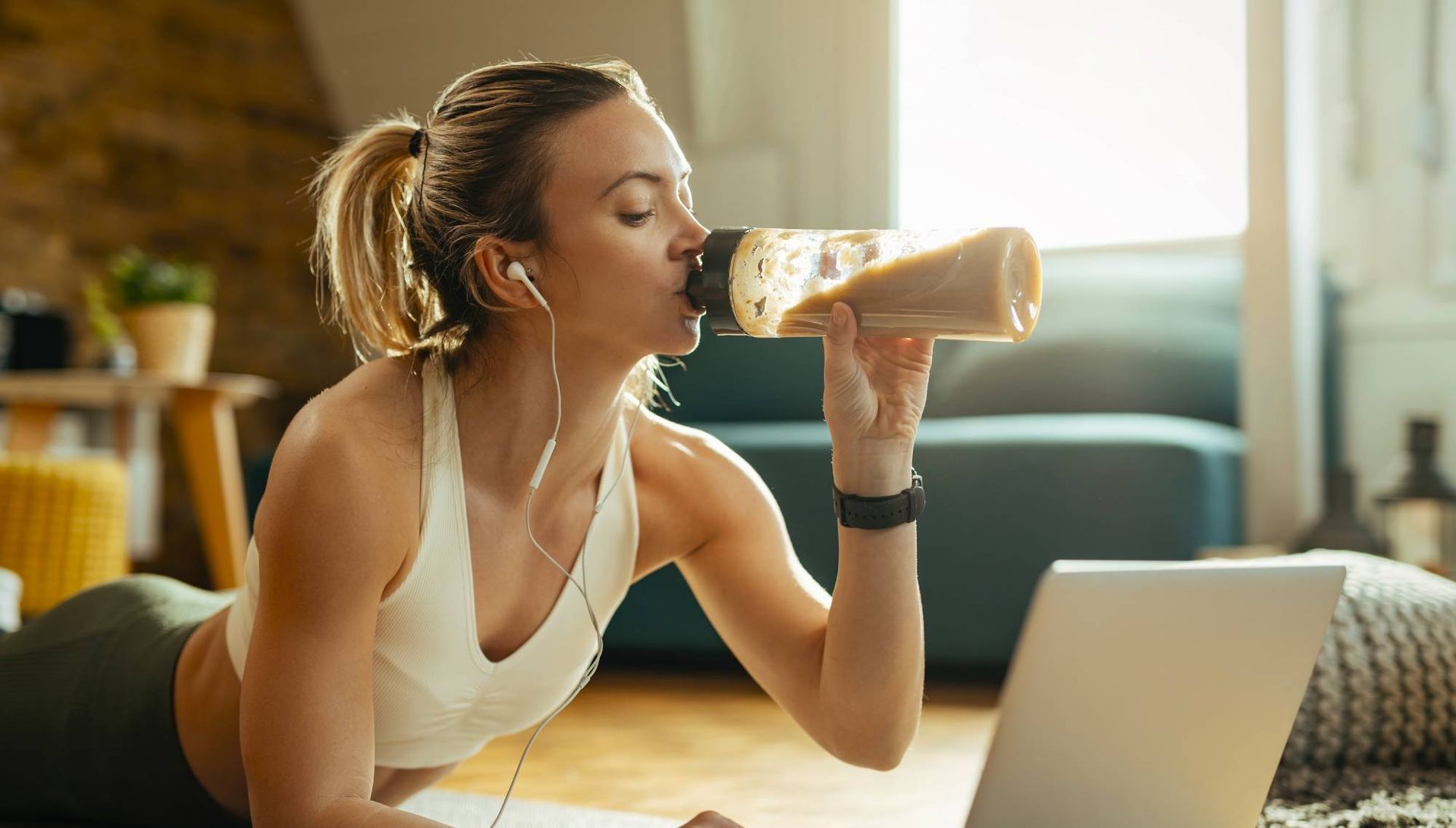 Una donna beve da una bottiglia mentre usa un computer portatile.
