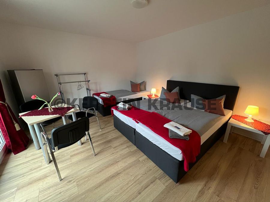 Schlafzimmer mit Doppelbett, Schreibtisch, Stuhl, Lampe und Koffer auf dem Boden