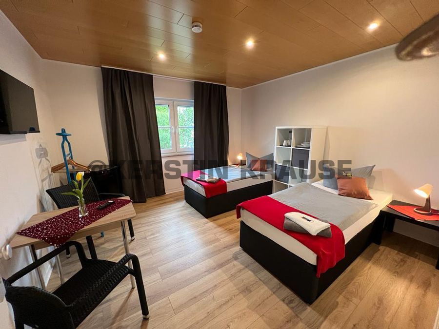 Schlafzimmer mit zwei Betten, Schreibtisch, Kleiderschrank und einem Fenster mit dunklen Vorhängen in einem holzgetäfelten Zimmer