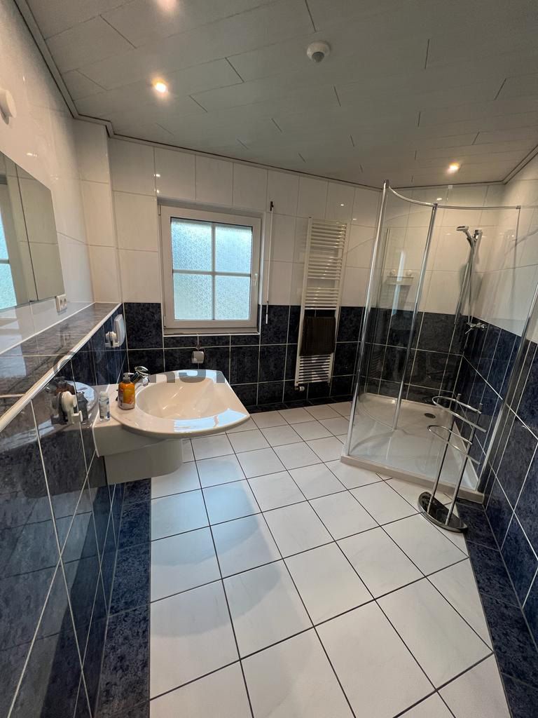 Modernes Badezimmer mit Waschbecken, Toilette, Duschkabine, weißem Fliesenboden und schwarzen Wandfliesen
