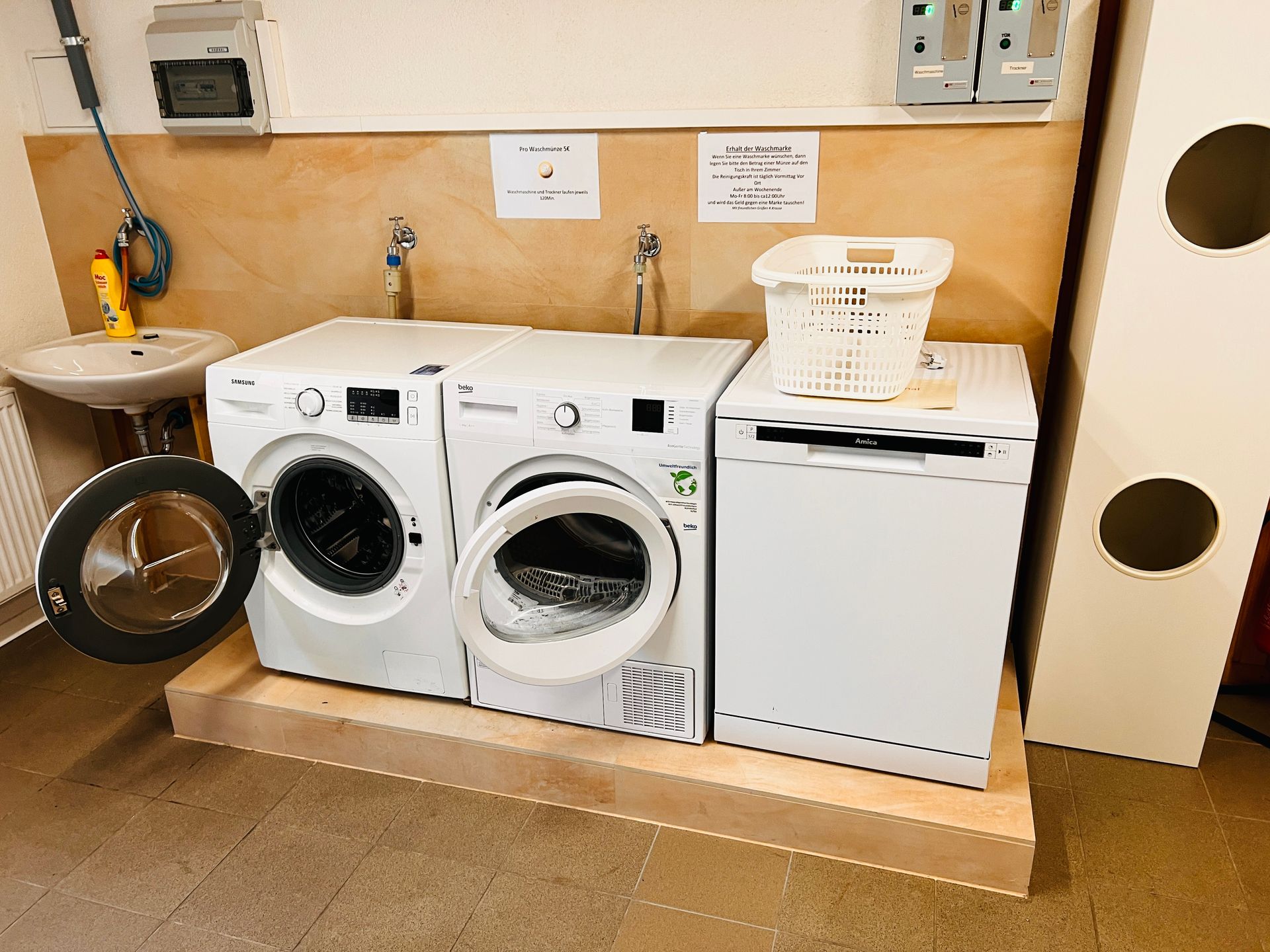 Waschküche mit Waschmaschine, Trockner und Aufsatzwaschbecken sowie einem Wäschekorb auf der Arbeitsfläche.