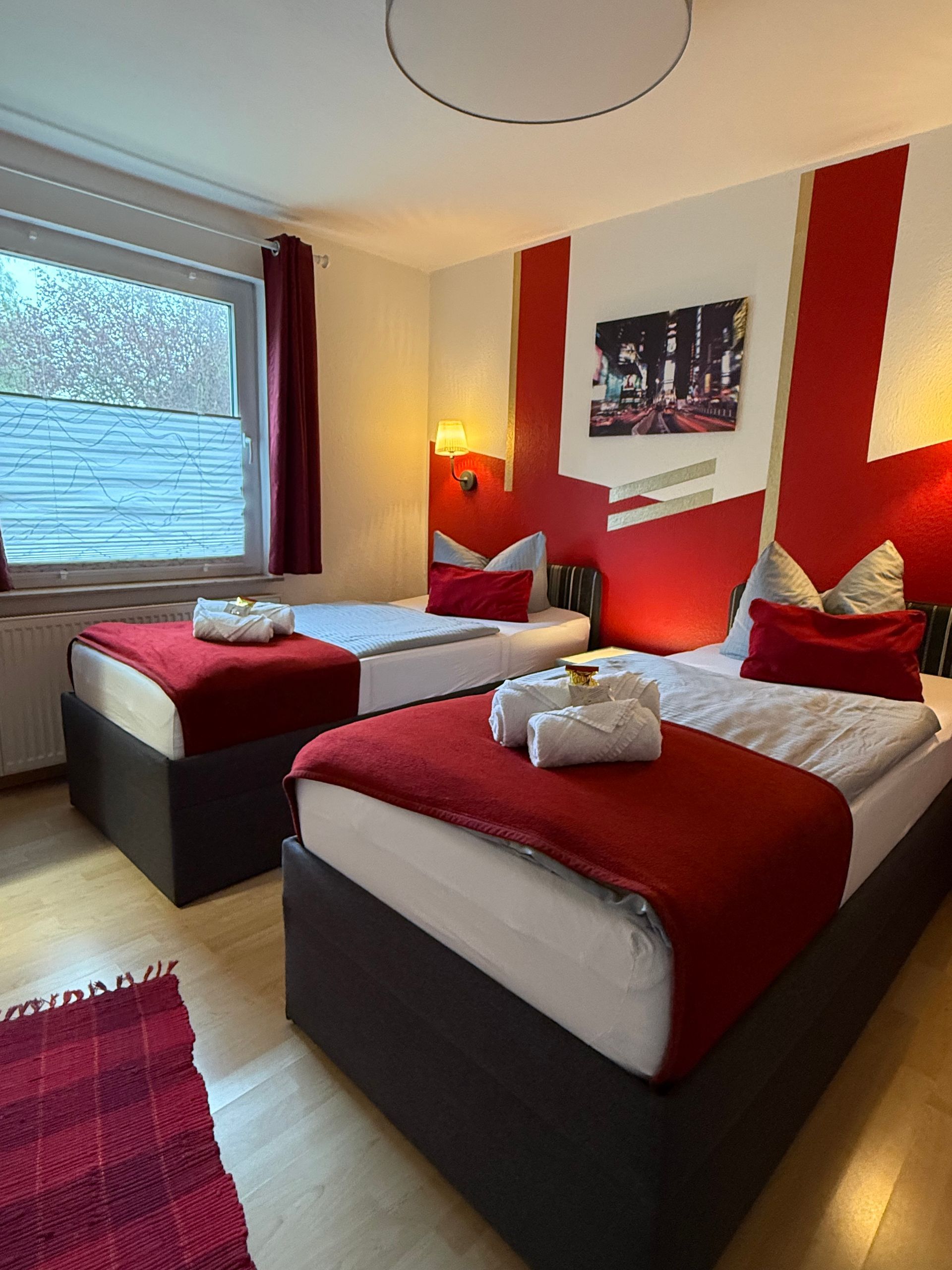 Zwei Einzelbetten mit rot-weißer Bettwäsche in einem hellen Hotelzimmer