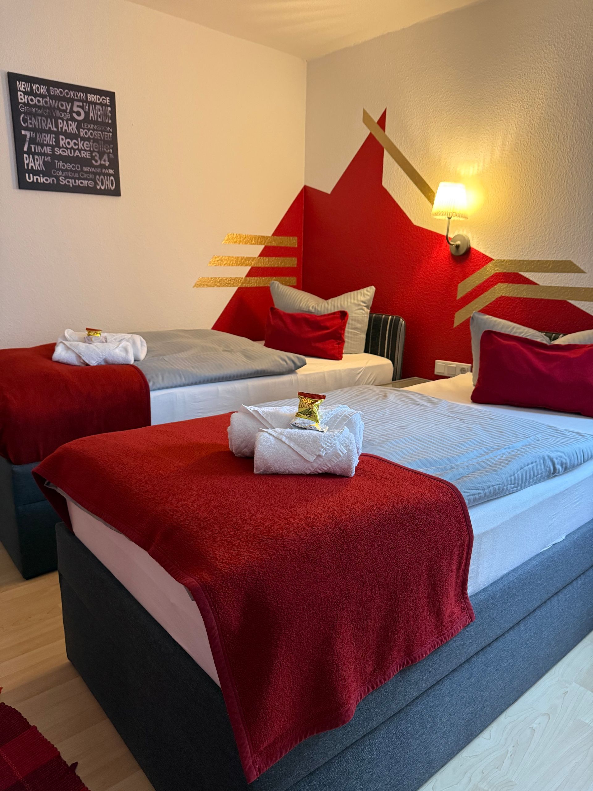 Zwei rot-weiße Betten in einem gemütlichen Hotelzimmer mit roter Akzentwand und warmem Lampenlicht.