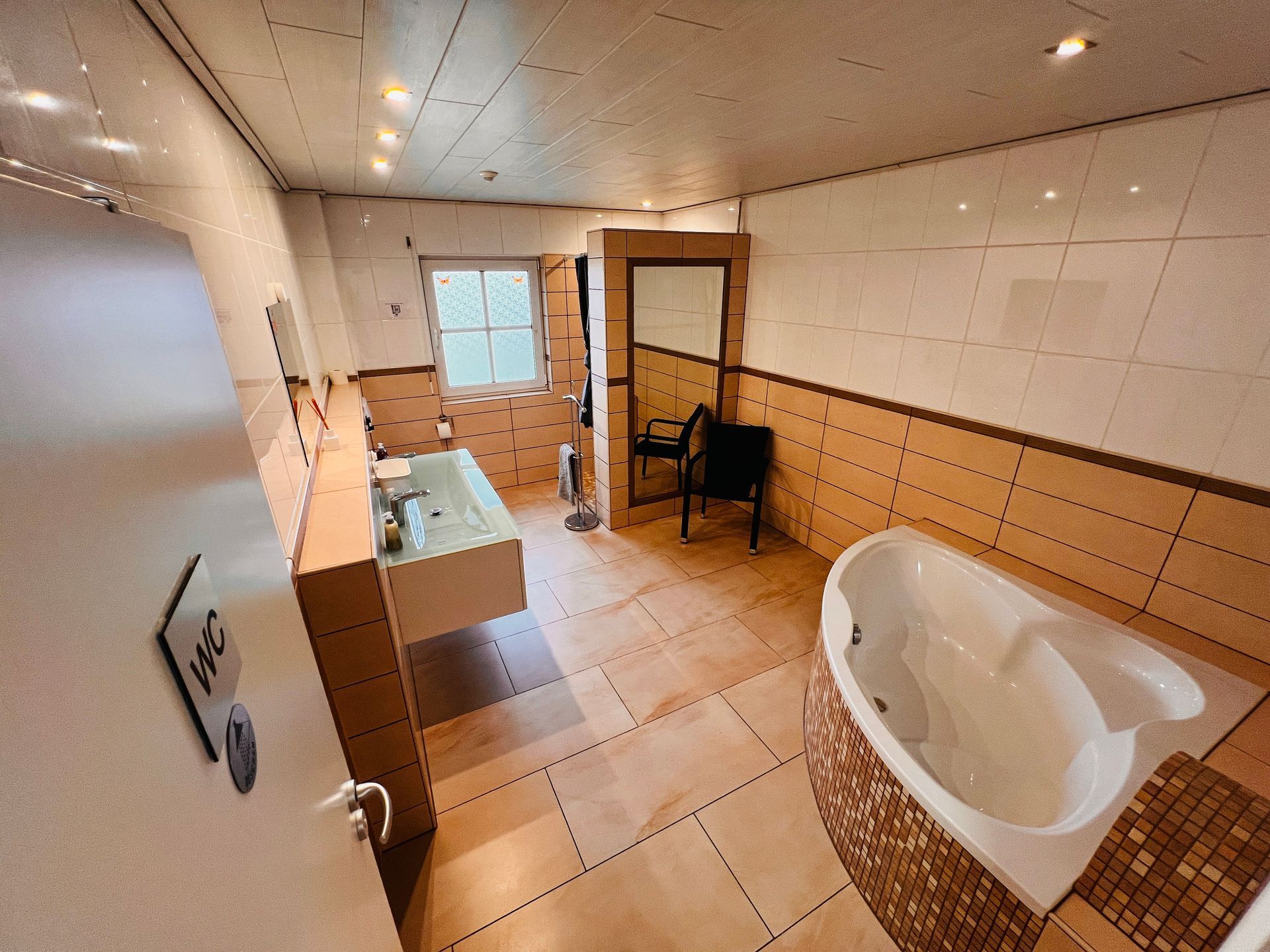 Modernes Badezimmer mit Badewanne, Waschbecken, Toilette und gefliesten Wänden in warmen Beigetönen.