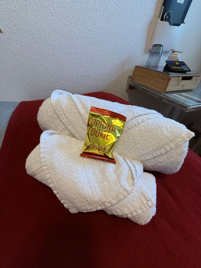 Weiße Handtücher auf einer roten Tagesdecke, darauf ein kleines gelbes Snackpäckchen.