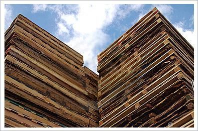 Paletas de madera apiladas contra un cielo azul parcialmente nublado.