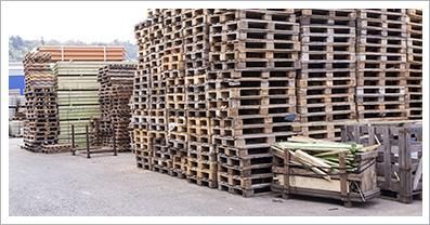 Pilas de palets de madera en un entorno al aire libre, probablemente un área de almacenamiento o industrial.