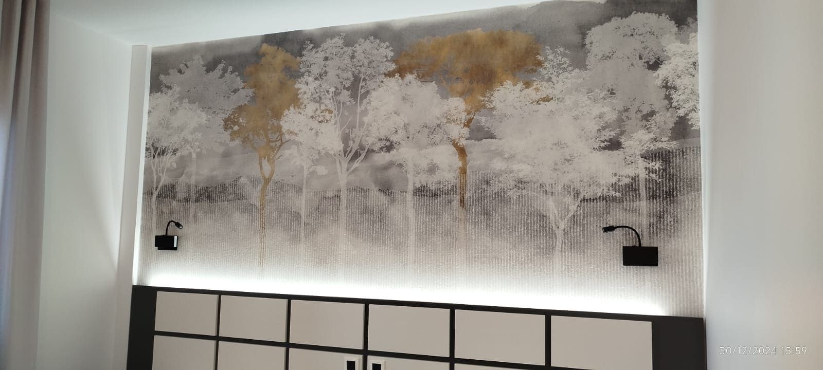 Pared de dormitorio con arte de un bosque blanco, iluminación cenital, apliques negros y cabecera blanca y negra.