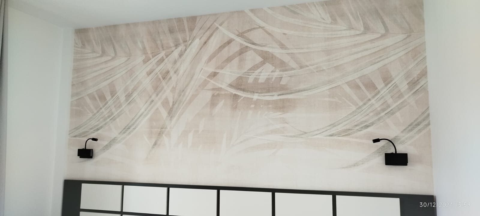 Pared del dormitorio con papel pintado estampado, dos lámparas de pared negras y un cabecero con paneles de espejo.