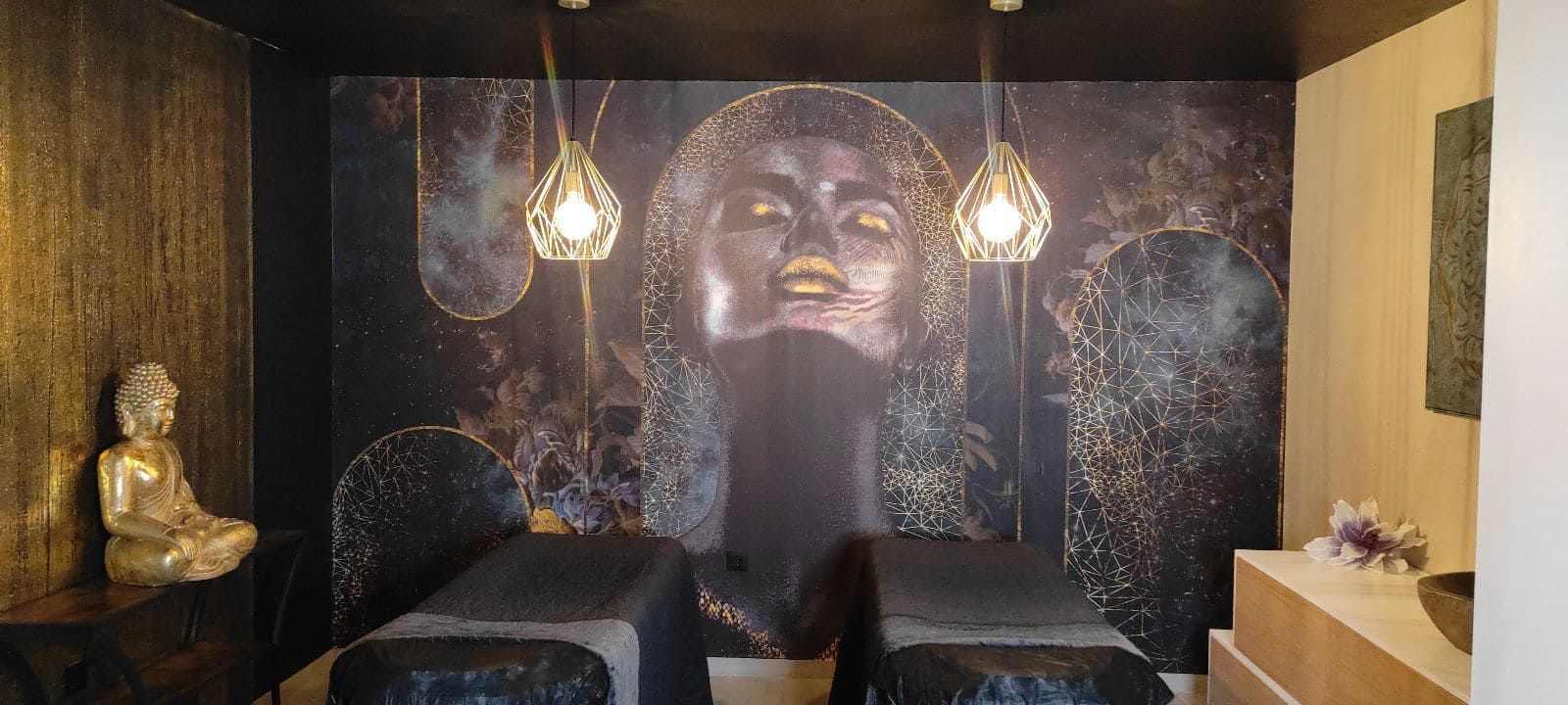 Una sala de spa con dos mesas de masaje, una estatua de Buda y un mural de pared de un rostro.
