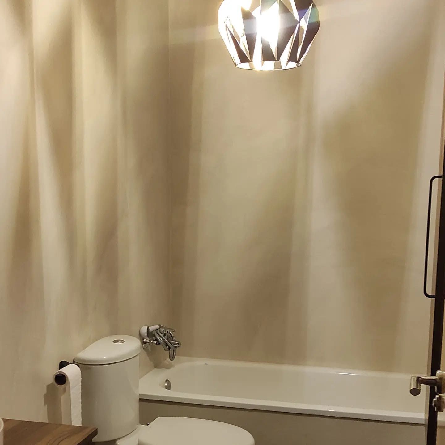 Un baño pequeño con inodoro, bañera y lámpara geométrica.