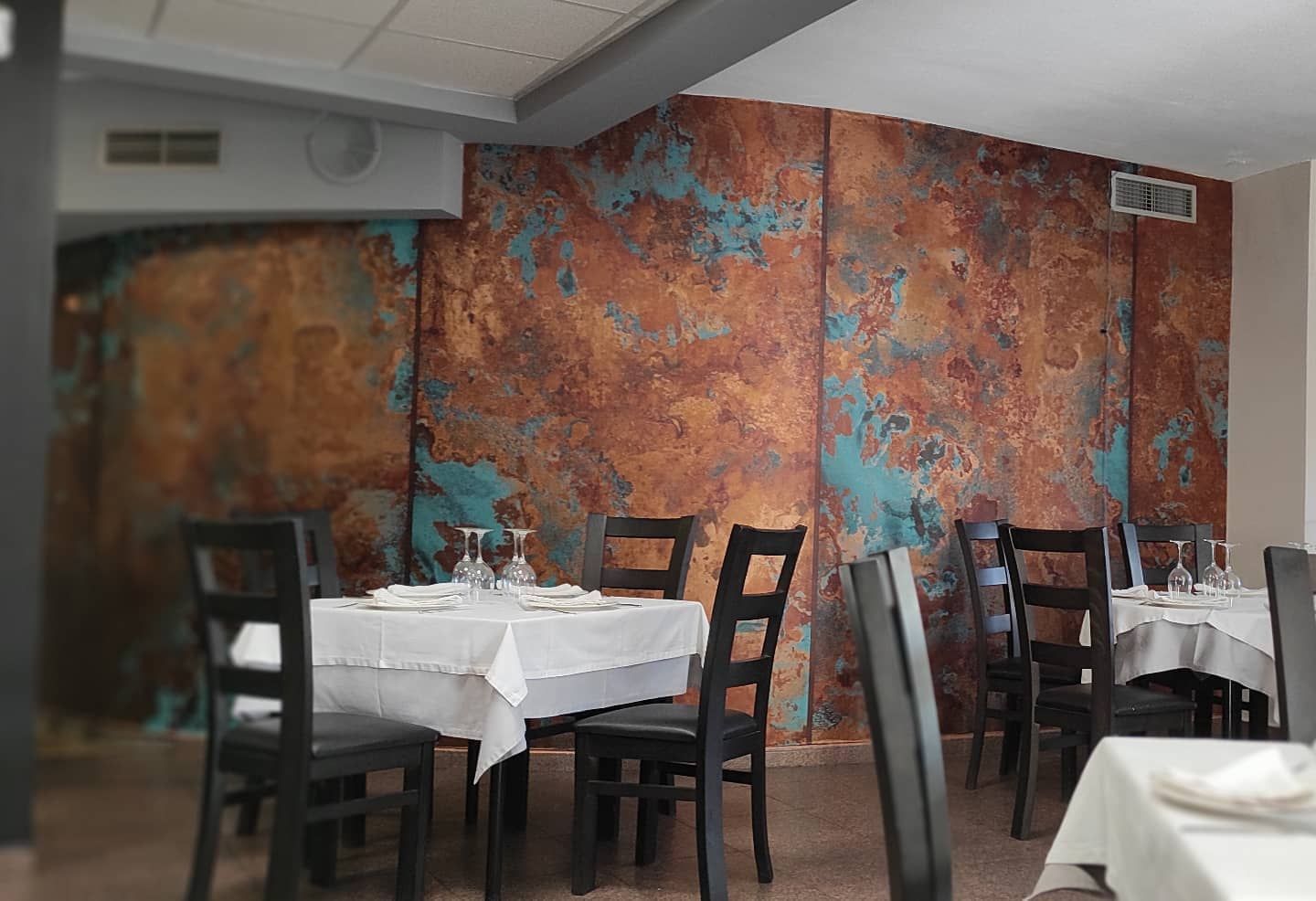 Interior de restaurante con mesas preparadas para cenar y una pared texturizada de color cobre.