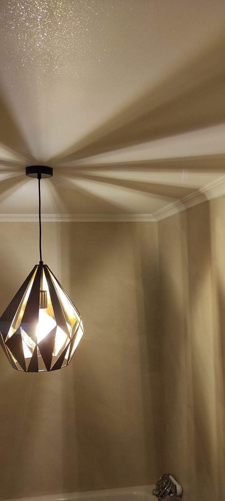 Una lámpara colgante en forma de diamante proyecta sombras en el techo y la pared de una habitación.