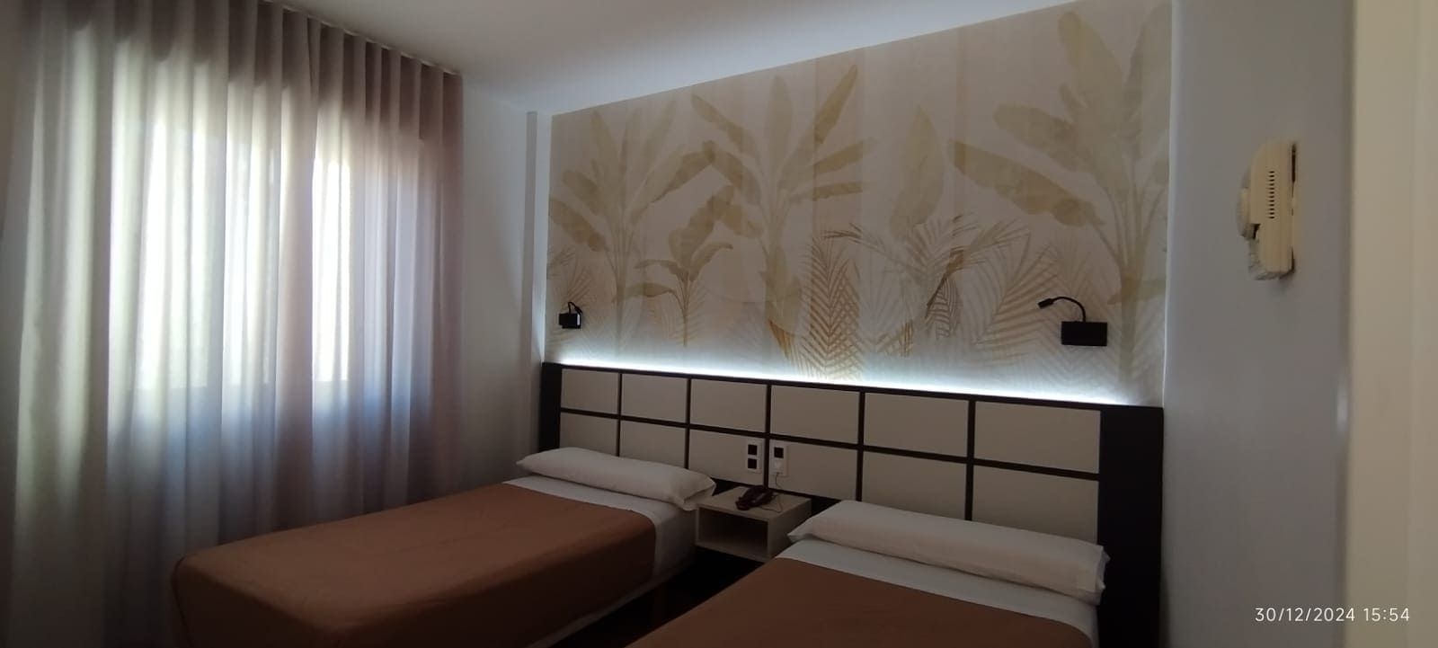 Camas individuales en un dormitorio con arte floral en la pared y cortinas.