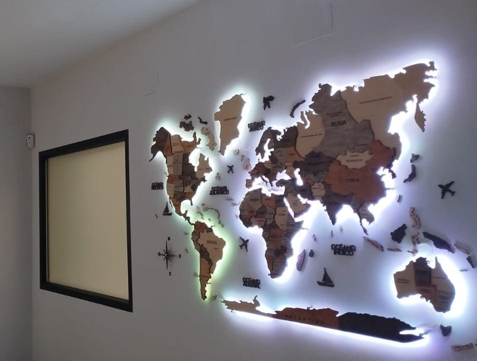 Un mapamundi de madera iluminado y su logotipo sobre una pared gris. Hay una ventana entre el mapa y el logotipo.